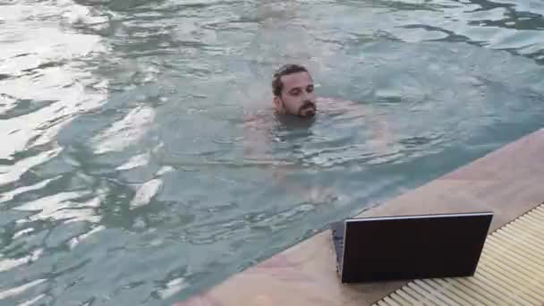 Jeune homme freelance bavarder avec ordinateur portable près de la piscine à l'hôtel — Video