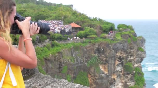 Vrouw staande op de rand van de kliffen in Uluwatu en nemen van foto 's — Stockvideo
