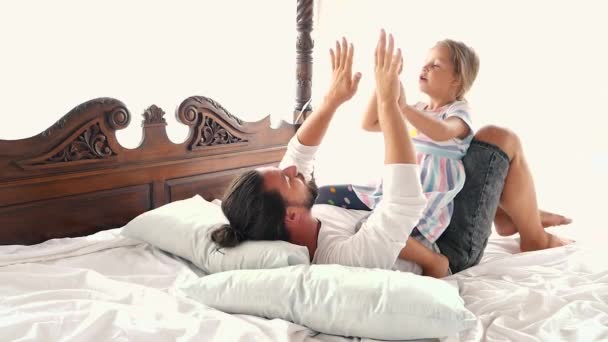 Feliz familia idilio hija pequeña saltar en los brazos del padre y caen en una cama — Vídeos de Stock