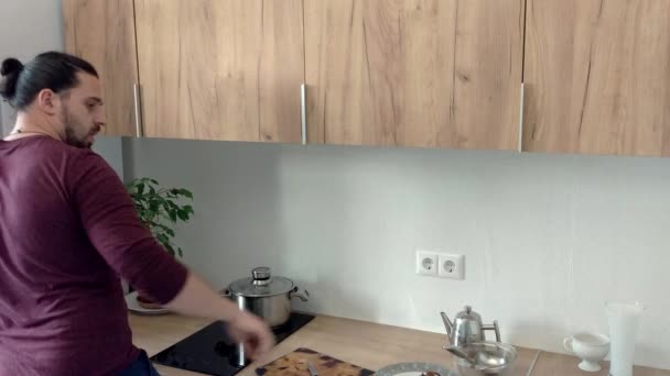 Atraktivní mladý legrační muž tančí a zpívá s naběračku, zatímco při vaření v kuchyni doma — Stock video