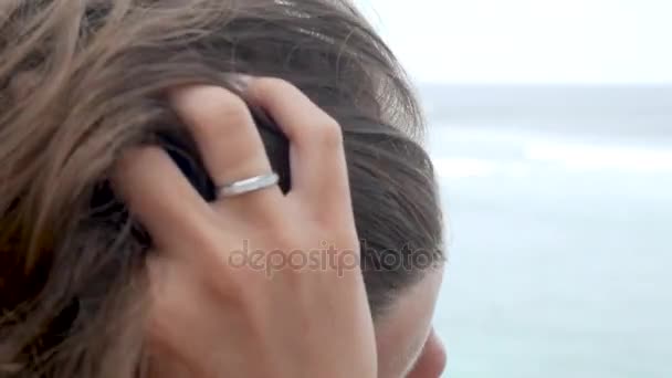 Junge schöne nachdenkliche Mädchen sitzt über dem Meer und schaut in den Horizont mit fliegenden Haaren im Wind — Stockvideo