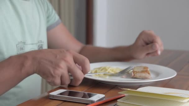 Young man using phone while eating breakfast — Stock Video