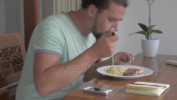 A fiatalember reggelizés közben a telefon használata — Stock videók