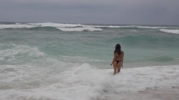 Mujer joven con elegante figura delgada está usando traje de baño abierto está caminando sobre una playa tropical — Vídeo de stock