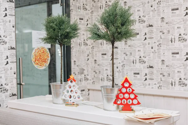 Gazete gibi stilize duvar kağıtları arka plan üzerinde küçük ağaçları ile metal backets yanında bir rafta duran iki dekoratif Noel ağaçları, kırmızı ve beyaz,.