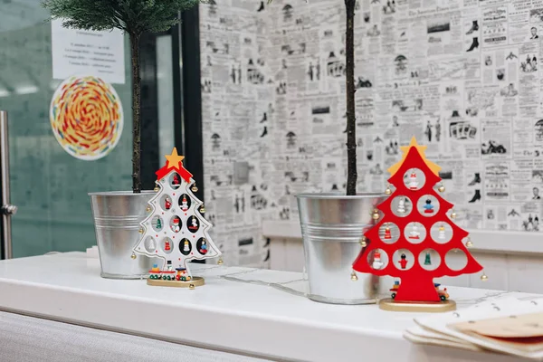 Gazete gibi stilize duvar kağıtları arka plan üzerinde küçük ağaçları ile metal backets yanında bir rafta duran iki dekoratif Noel ağaçları, kırmızı ve beyaz,.