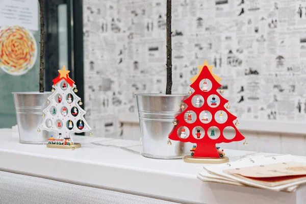 Gazete gibi stilize duvar kağıtları arka plan üzerinde küçük ağaçları ile metal backets yanında bir rafta duran iki dekoratif Noel ağaçları, kırmızı ve beyaz,.