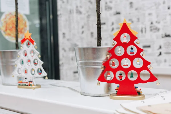Gazete gibi stilize duvar kağıtları arka plan üzerinde küçük ağaçları ile metal backets yanında bir rafta duran iki dekoratif Noel ağaçları, kırmızı ve beyaz,.