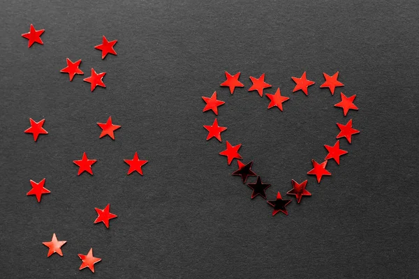 A heart made of small red stars accompanied by some more red stars placed on a black matte backdrop