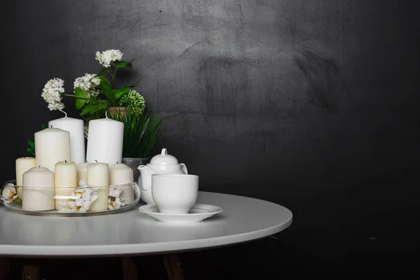 Beyaz bir sehpa ile beyaz bardak ve çay potu, beyaz mumlar, bazı yeşil çim ve flowers.loft tasarım