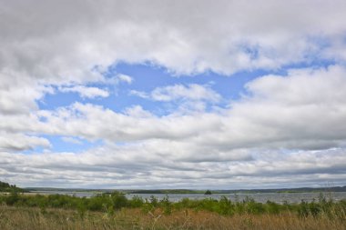 Kümülüs ve yırtık pırtık sirrus bulutları göl üzerinde mavi bir gökyüzünde. Kopyalama alanı olan doğal yaz arkaplanı