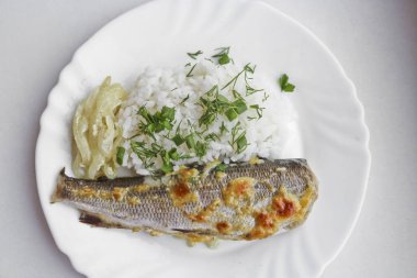 Haşlanmış pirinçli fırında balık ve beyaz bir tabakta kızarmış soğan. Sağlıklı diyet yemekleri.