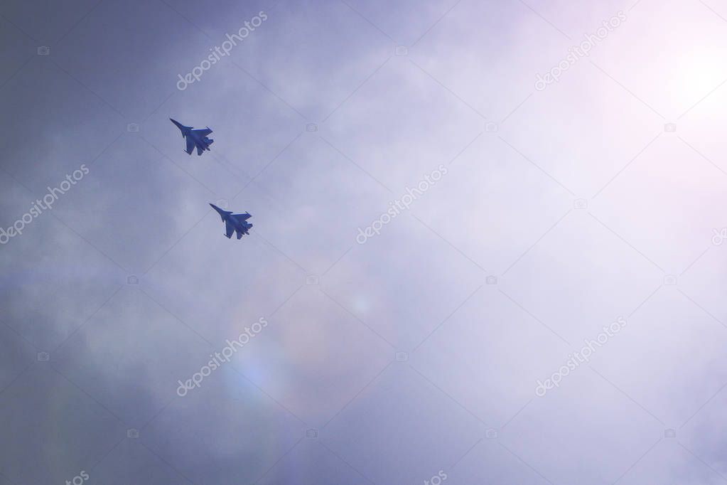 Two military fighters fly in the sky. Behind them stretches a co