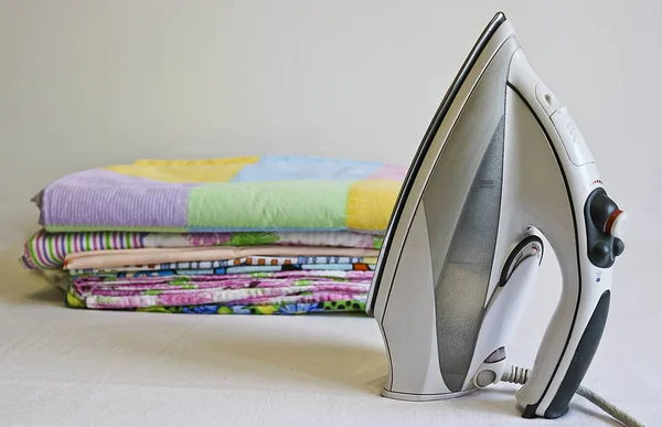 Modern iron and stack of ironed linen. Household chores.