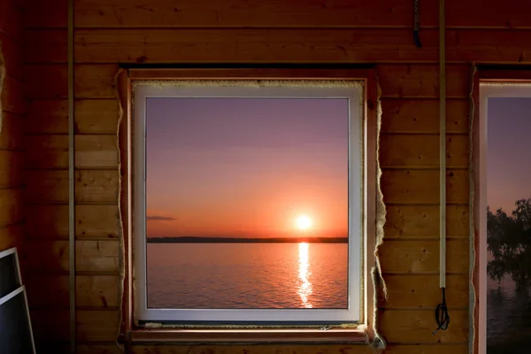 The view from the window of a wooden country house on a colorful sunset over the lake. Summer house on the shore of the reservoir. Calmness and relaxation.
