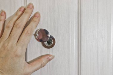 Bir kadın eli ön kapıdaki kapı deliğinin panjurunu açıyor. Güvenlik ve ihtiyat kavramı.