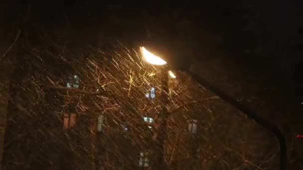 Swiftly flying wet snow in the light of a street lamp. Blizzard on a spring night. Beautifully lit jets of rain. — Stock Video