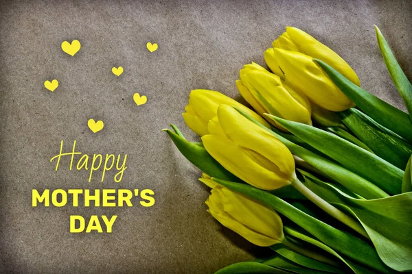 Greeting card Happy Mother's Day. With the inscription Happy Mother's Day. Bright yellow tulips on rough brown paper.
