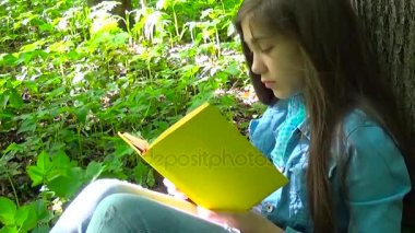 Genç kız kitap ve ormandaki ağaç gövdesi karşı ilkbaharda, eğilerek dönüm sayfa okuma açık eğitim portresi. İlk ciddi, sonra güler.