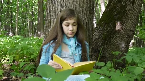 Portret van ernstige tienermeisje lezen boek en draaien pagina leunend tegen boomstam in het bos in het voorjaar, studeren buiten. — Stockvideo