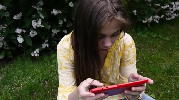 Mooie tiener meisje met tablet pc zit op het gras in het Park. Film van statische camera. — Stockvideo