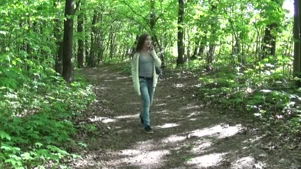 Atractiva chica adolescente hablando en el teléfono móvil mientras camina en el hermoso parque de primavera . — Vídeos de Stock