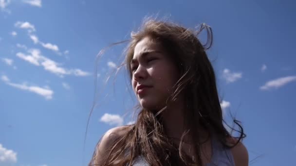 Close up portrait of beautiful young girl on the blue sky background with blowing hair in wind — Stock Video