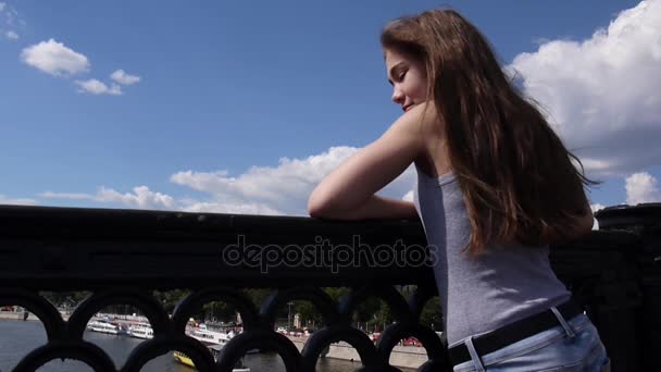 Retrato de una hermosa joven en el puente de fondo cielo azul con el pelo soplado en el viento — Vídeos de Stock