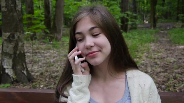 Joven chica atractiva hablar por teléfono en el banco. Parque de verano. Sonríe. Vídeo HD filmación de la cámara estática . — Vídeos de Stock