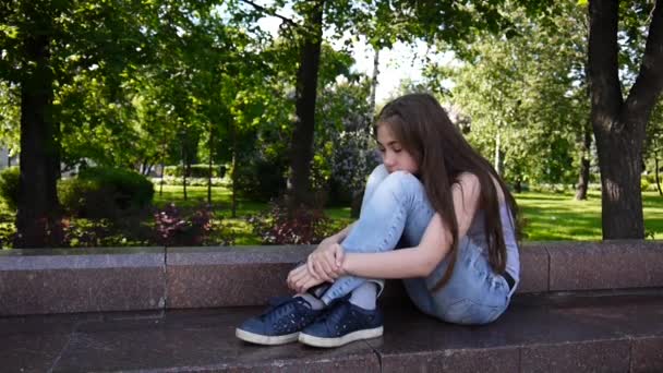 Schattige tienermeisje controleren telefoon en wachten telefoongesprek zitten in park. Videobeelden Hd schieten statische camera. — Stockvideo