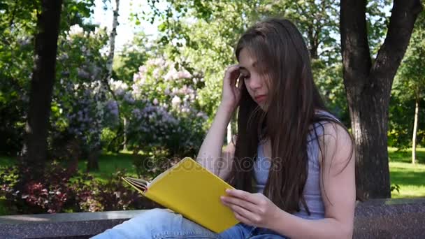 Linda adolescente leyendo libro sentado en el banco en el parque, estudiando al aire libre. Vídeo HD filmación de la cámara estática . — Vídeos de Stock