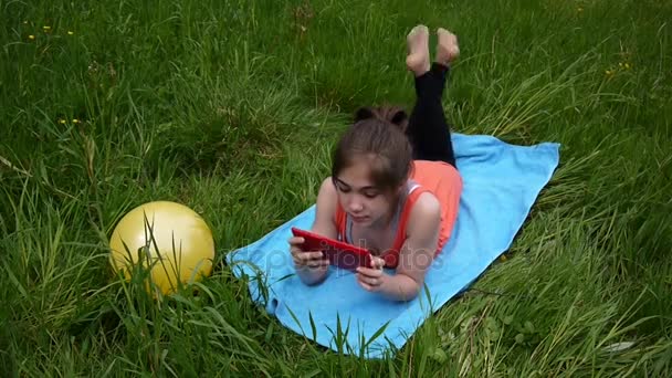 Entspanntes junges Mädchen mit digitalem Tablet auf dem Land. niedlichen Teenager auf dem Gras liegend. Videomaterial hd Aufnahme von statischer Kamera. — Stockvideo