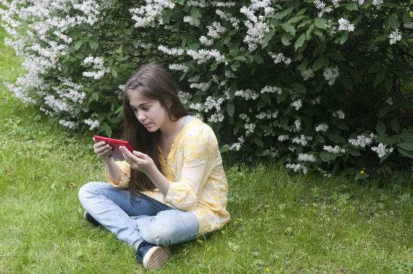 Menina adolescente bonita com computador tablet senta-se na grama no Parque. Foto — Fotografia de Stock