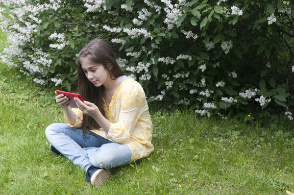 Menina adolescente bonita com computador tablet senta-se na grama no Parque. Foto — Fotografia de Stock