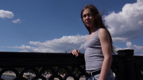 Portret van mooie jonge meisje op de achtergrond van de blauwe hemel brug met haren in de wind waait — Stockvideo