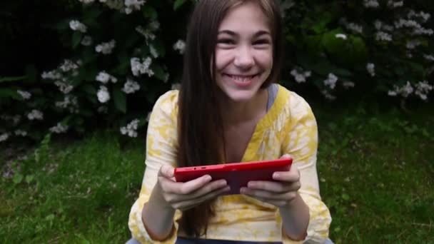 Hermosa chica adolescente con tableta se sienta en la hierba en el parque. Película de cámara estática . — Vídeos de Stock