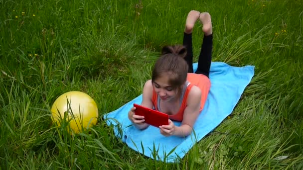 轻松的年轻女孩使用数字平板在农村领域。可爱的青少年躺在草地上。静态摄像机高清拍摄录像. — 图库视频影像