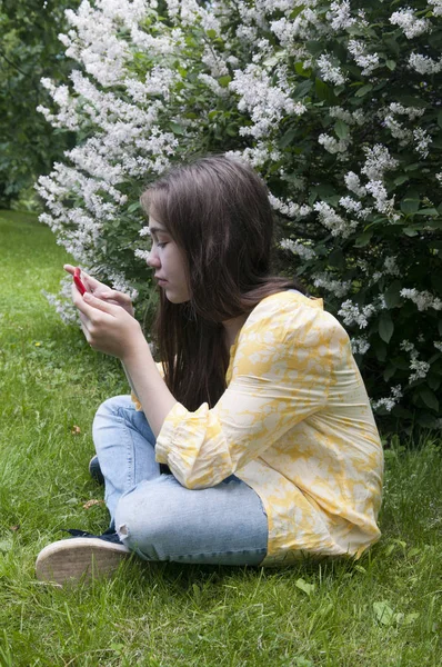 Красивая девочка-подросток с планшетным компьютером сидит на траве в парке. Фото — стоковое фото