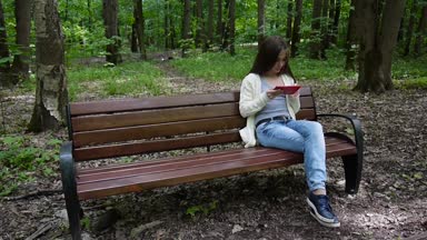 Güzel genç kız tablet bilgisayar ile parkta bankta oturur. Statik kamera film.