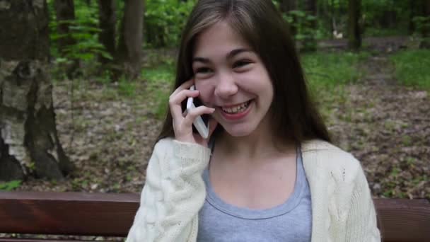 Joven chica atractiva hablar por teléfono en el banco. Parque de verano. Sonríe. Vídeo HD filmación de la cámara estática . — Vídeo de stock