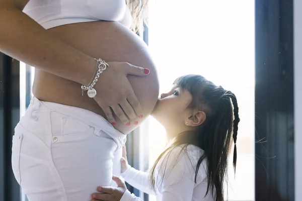 Niña besando a su madre vientre embarazada . — Foto de Stock