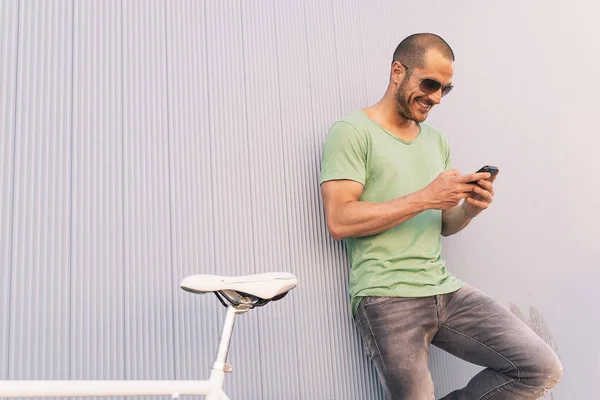 ชายหนุ่มหล่อที่มีโทรศัพท์มือถือและจักรยานเกียร์คงที่ . — ภาพถ่ายสต็อก