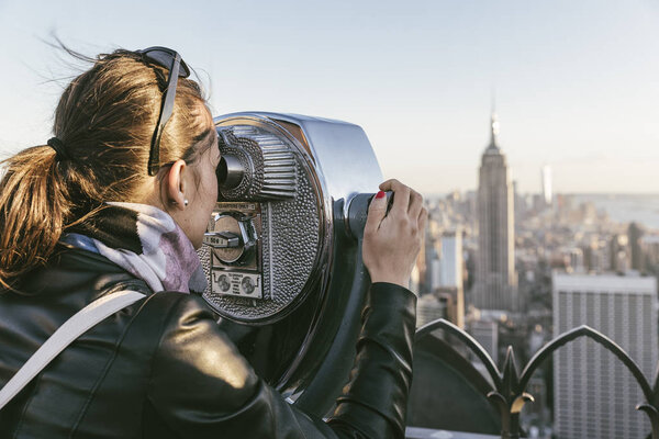 Tourist woman using binoculars in rooftop. New York Concept.