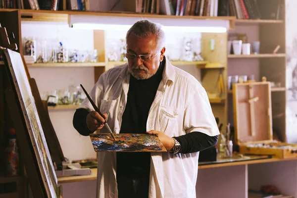 Velho artista pintando óleos em seu estúdio . — Fotografia de Stock