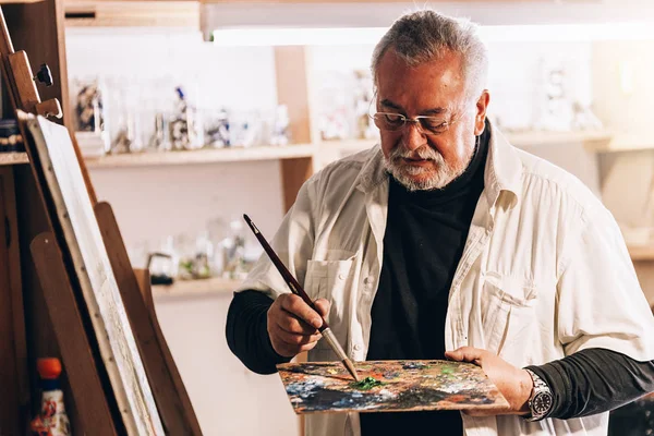 Velho artista pintando óleos em seu estúdio . — Fotografia de Stock