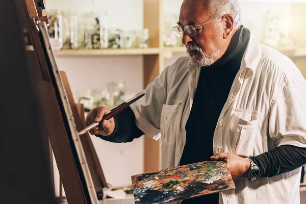 Velho artista pintando óleos em seu estúdio . — Fotografia de Stock