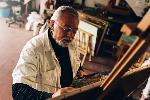 Velho artista pintando óleos em seu estúdio . — Fotografia de Stock