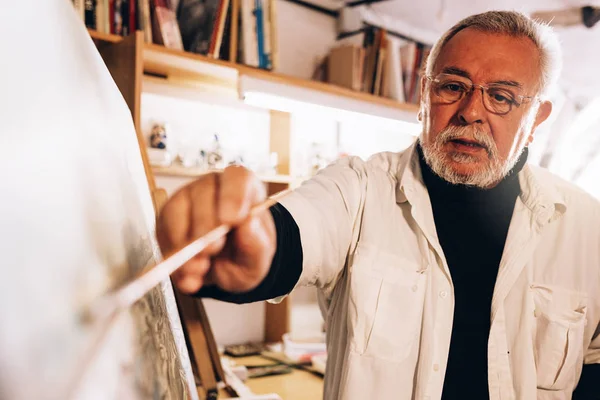 Vieil homme artiste peinture à l'huile dans son atelier . — Photo