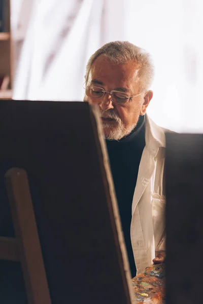 Old man artist painting oils in his studio. — Stock Photo, Image