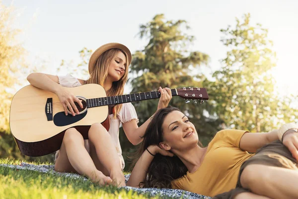 Piękne kobiety, zabawy gry na gitarze w parku. — Zdjęcie stockowe